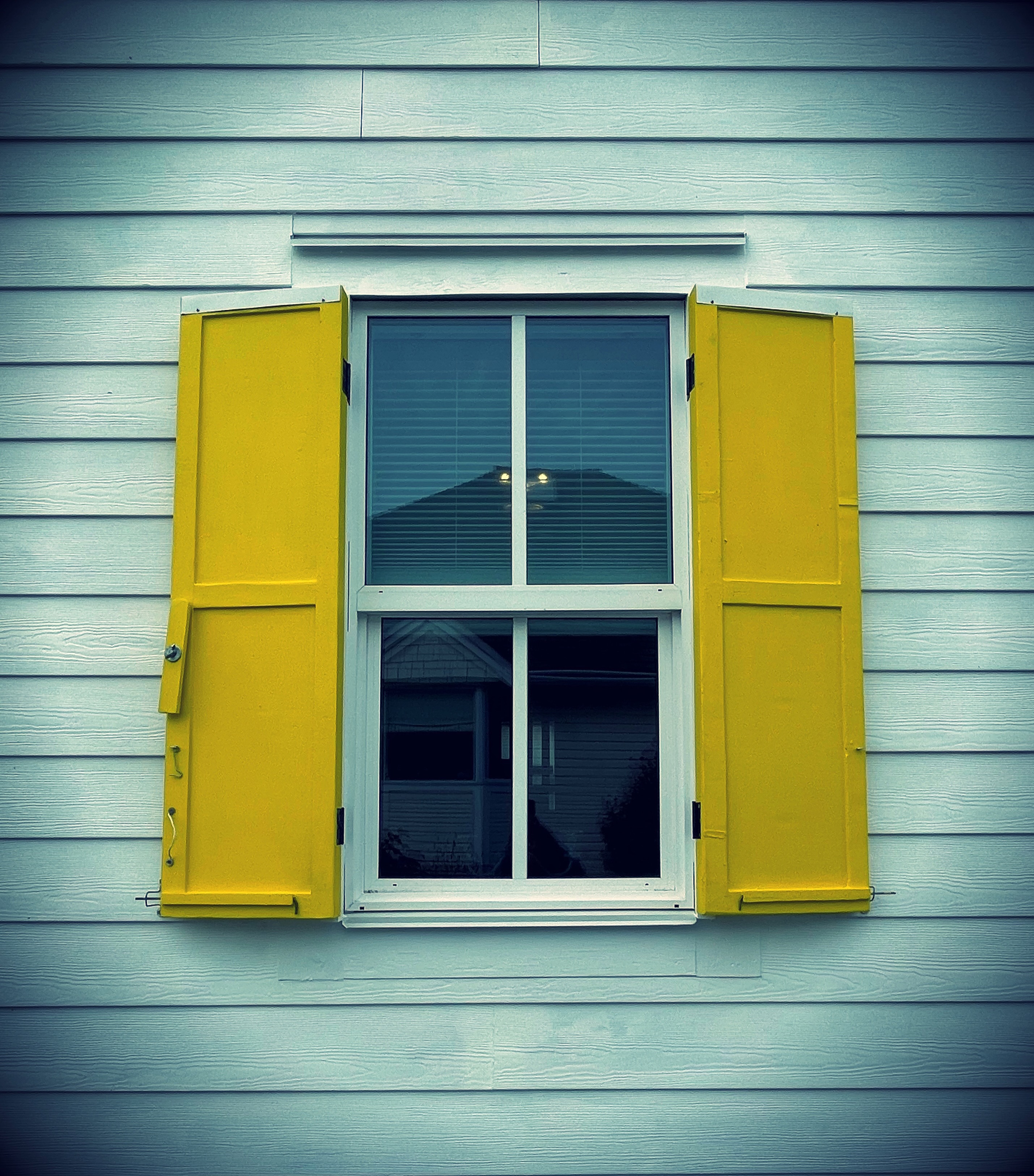 A window with yellow shutters on a blue house.